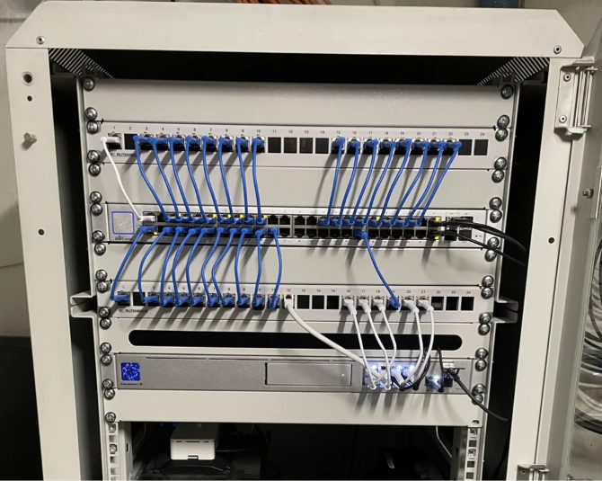 A wall-mounted UniFi network rack with patch panel, switch and gateway